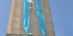 Hombre descendiendo por fuera de la torre del Monumento donde se despliega una larga bandera
