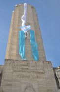 Hombre descendiendo por fuera de la torre del Monumento donde se despliega una larga bandera